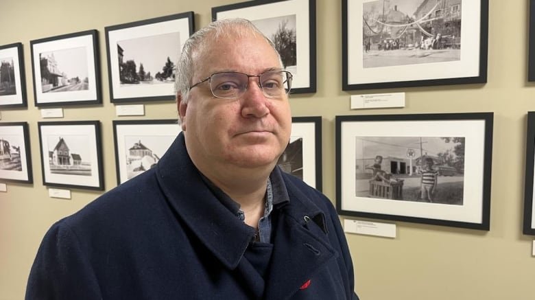 A man in a blue jacket poses for a photo in front of a wall of photos