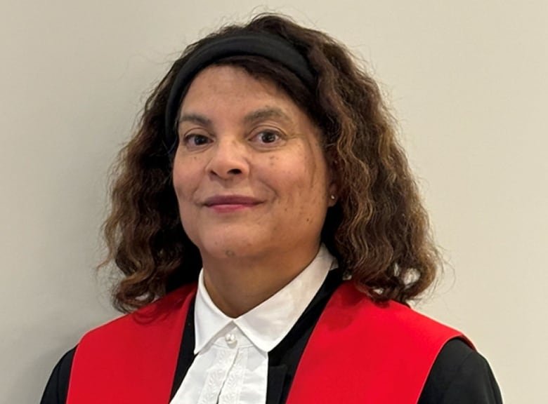 A woman is shown wearing black and red judge's robes.