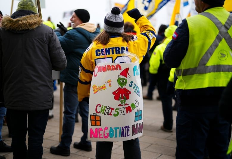 A woman in a crowd wears a sign with a drawing of the Grinch. It reads "don't steal Christmas" and "negotiate now."