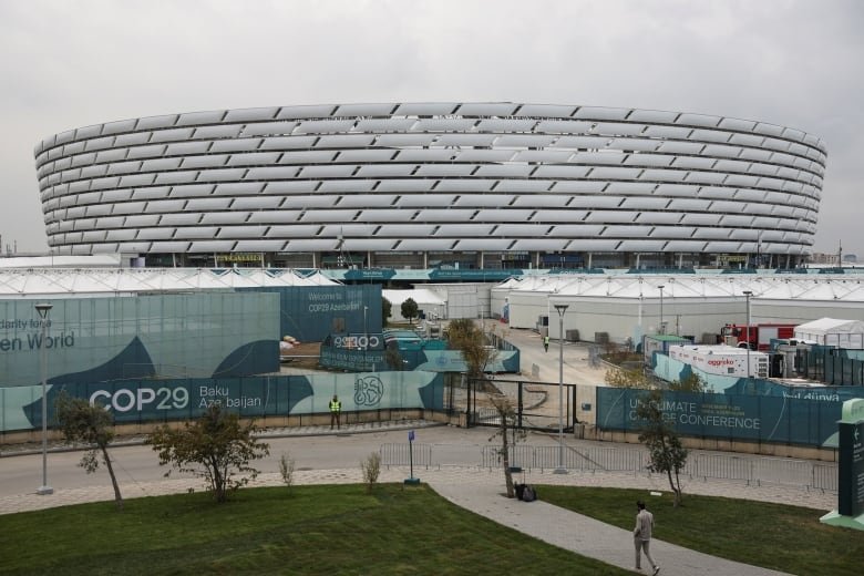 A building shaped like a pie plate with white bricks seen from the side, with signs for 'COP29'