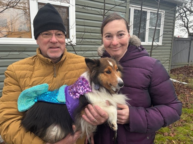 A man and woman holding a dog in a yard.