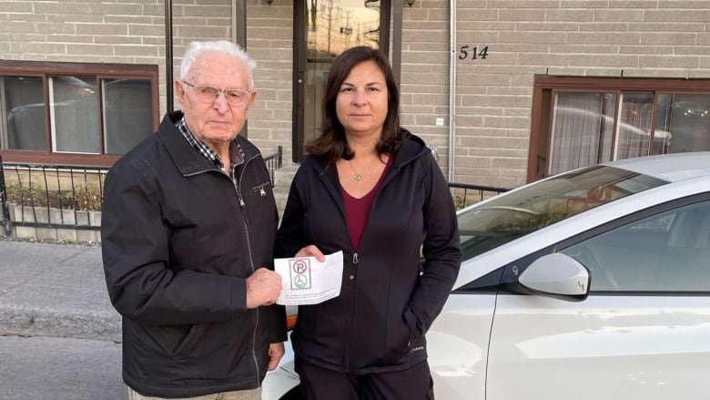 Two people look angry holding a piece of paper with a no parking and handicapped parking sign.