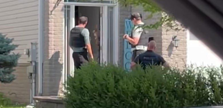 Three officers stand outside an open door at a house.