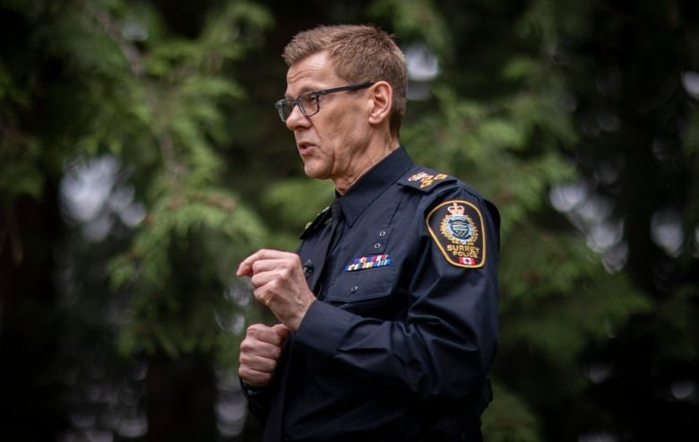 A white man wearing a police uniform gestures while speaking in a park.