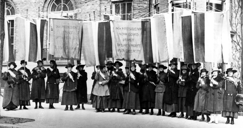 Suffragettes march with signs.