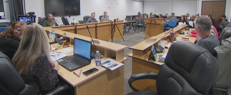 A number of people sit around long, brown desks at a planning board meeting.