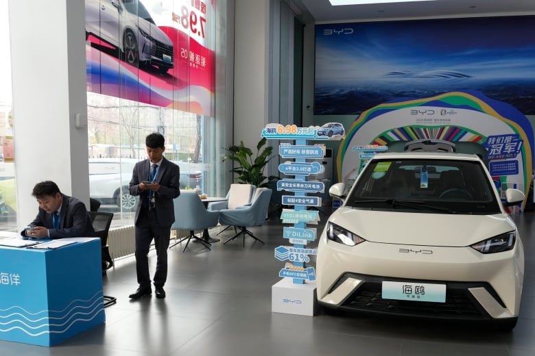 Sales staff stand near the Seagull electric vehicle from Chinese automaker BYD at a showroom in Beijing, Wednesday, April 10, 2024. The tiny, low-priced electric vehicle called the Seagull has American automakers and politicians trembling. The car, launched last year by Chinese automaker BYD, sells for around $12,000 in China. But it drives well and is put together with craftsmanship that rivals U.S.-made electric vehicles that cost three times as much. Tariffs on imported Chinese vehicles probably will keep the Seagull away from America’s shores for now.