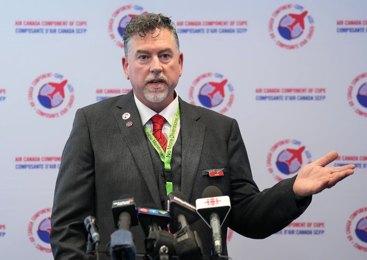 A man in a suit speaks into a set of microphones.