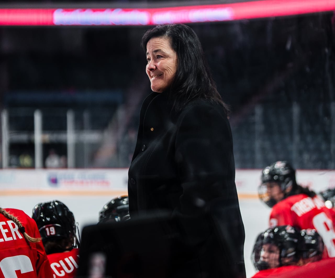 A woman stands behind a hockey bench.