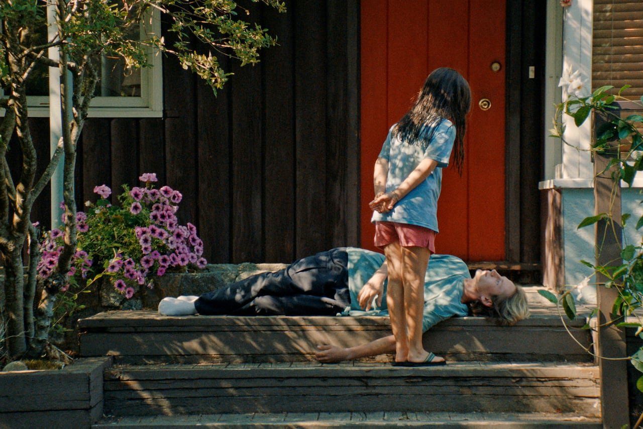 A young girl stands over a young man lying on a stoop.