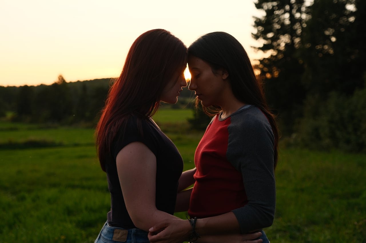Two women embrace in front of a sunset.