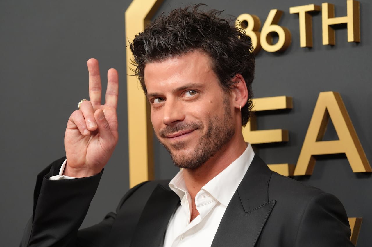 A man in a dark grey suit smiles and flashes a peace sign